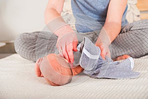 Father dresses a newborn in the bedroom. Clothes baby undershirts and sliders on a baby close-up and copy space. Home care and bab