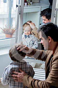 Father dressing up a toddler boy near window at home