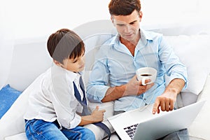 Father drinking coffee and teaching son how to use notebook.