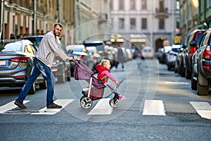 Father drives child in perambulator along pedestrian crossing.