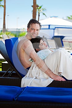 Father drying off on blue lounger with disabled son off side of