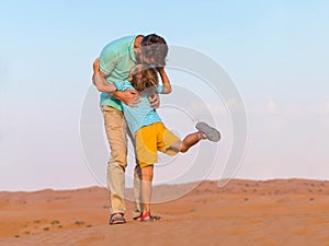 Father embraces the little son on a travel on the boundless desert. Orange sand,