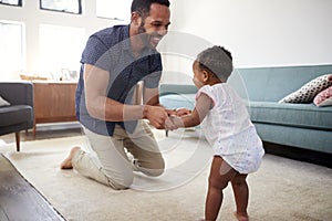 Father Encouraging Baby Daughter To Take First Steps At Home