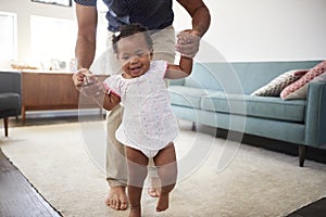 Father Encouraging Baby Daughter To Take First Steps At Home
