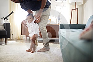 Father Encouraging Baby Daughter To Take First Steps At Home