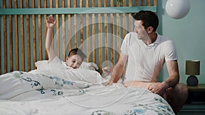 A father enters into the bedroom to sleeping son, wakes him up, indicating that it is already morning, a boy stretches