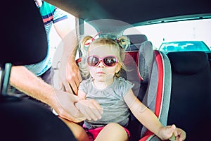 Father fasten blondy baby daughter 2-3 year old in car seat standing on parking. Transport, safety, childhood road trip and people