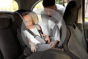 Father fastening his sleeping daughter with car safety seat belt