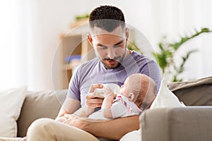 Father feeding baby daughter from bottle at home