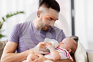 Father feeding baby daughter from bottle at home