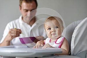 Father feeding baby daughter in high chair