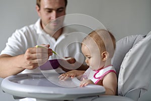 Father feeding baby daughter in high chair
