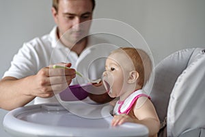 Father feeding baby daughter in high chair