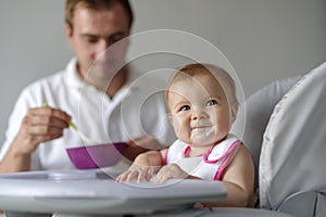 Father feeding baby daughter in high chair