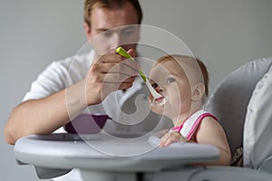 Father feeding baby daughter in high chair