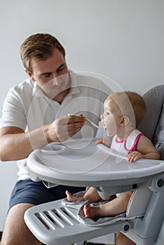 Father feeding baby daughter in high chair