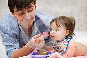 Father feeding baby girl on blanket at home