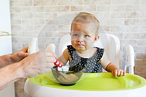 Father feeding baby girl at home in the kitchen