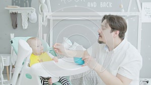 Father feeding baby sitting on high chair at home