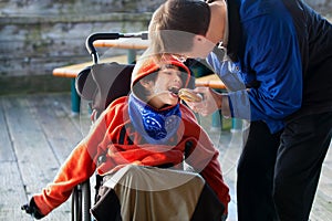 Father feeding disabled son a hamburger in wheelchair. Child has