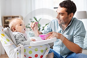 Father feeding happy baby in highchair at home