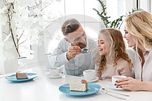 father feeding his daughter with cake while they spending time