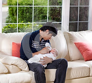 Father feeding his infant son on white sofa