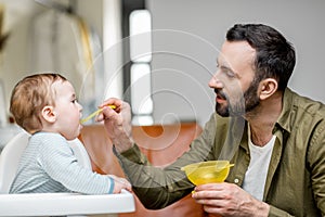 Father feeding his one year baby boy with a spoon.