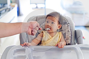 Father feeding porridge to his kid on baby feeding seat.