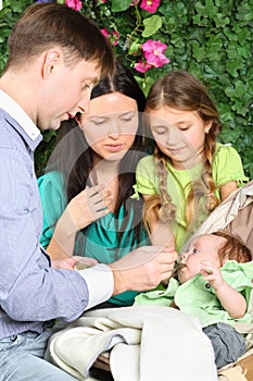 Father feeds baby and mother and little daughter look at baby