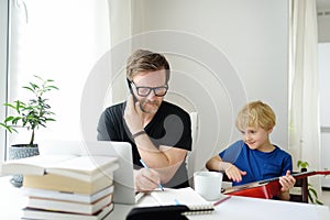 Father freelancer working from home with laptop during quarantine. Naughty son distracts. Home office and parenthood at same time