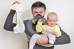 Father with gas mask is holding dirty diaper and little baby