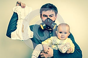 Father with gas mask is holding dirty diaper and little baby