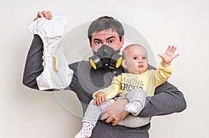 Father with gas mask is holding stinky diaper and little baby