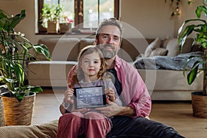 Father and girl holding smart thermostat, adjusting, lowering heating temperature at home. Concept of sustainable