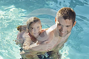 Father Giving Daughter Piggyback In Swimming Pool