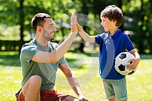 Father giving five to son with soccer ball at park