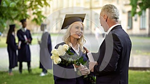 Father giving flowers to his graduate daughter, congratulations, paternal pride photo