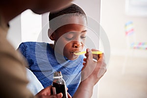 Father Giving Sick Son Ill In Bed Medicine From Bottle