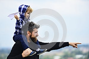 Father giving son ride on back in park. Father and son building together a paper airplane. Happy child playing with toy