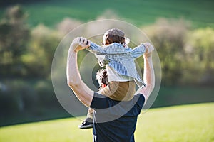 A father giving toddler son piggyback ride outside in spring nature.