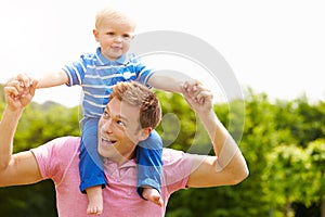 Father Giving Young Son Ride On His Shoulders In Garden