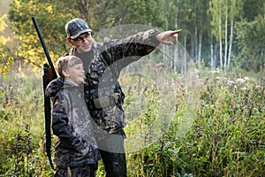 Father with gun showing something to son while hunting on a nature.