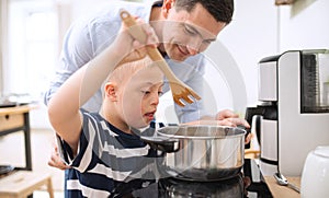 Father with happy down syndrome son indoors in kitchen, cooking.