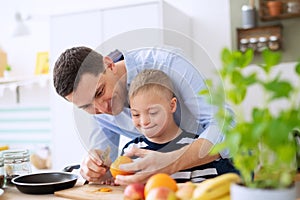Father with happy down syndrome son indoors in kitchen, preparing food.