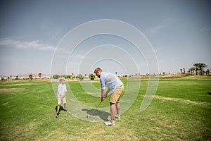 Father has fun and teaches his son to play golf on the green grass