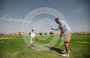 Father has fun and teaches his son to play golf on the green grass