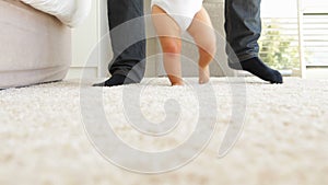 Father helping baby to walk across rug