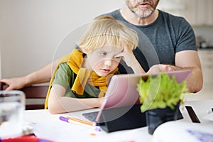 Father helping child do homework at home. Tired child does not understand. Homeschooling, distance learning, online studying,