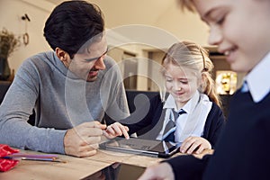 Father Helping Children Using Digital Tablets Wearing School Uniform With Homework At Table